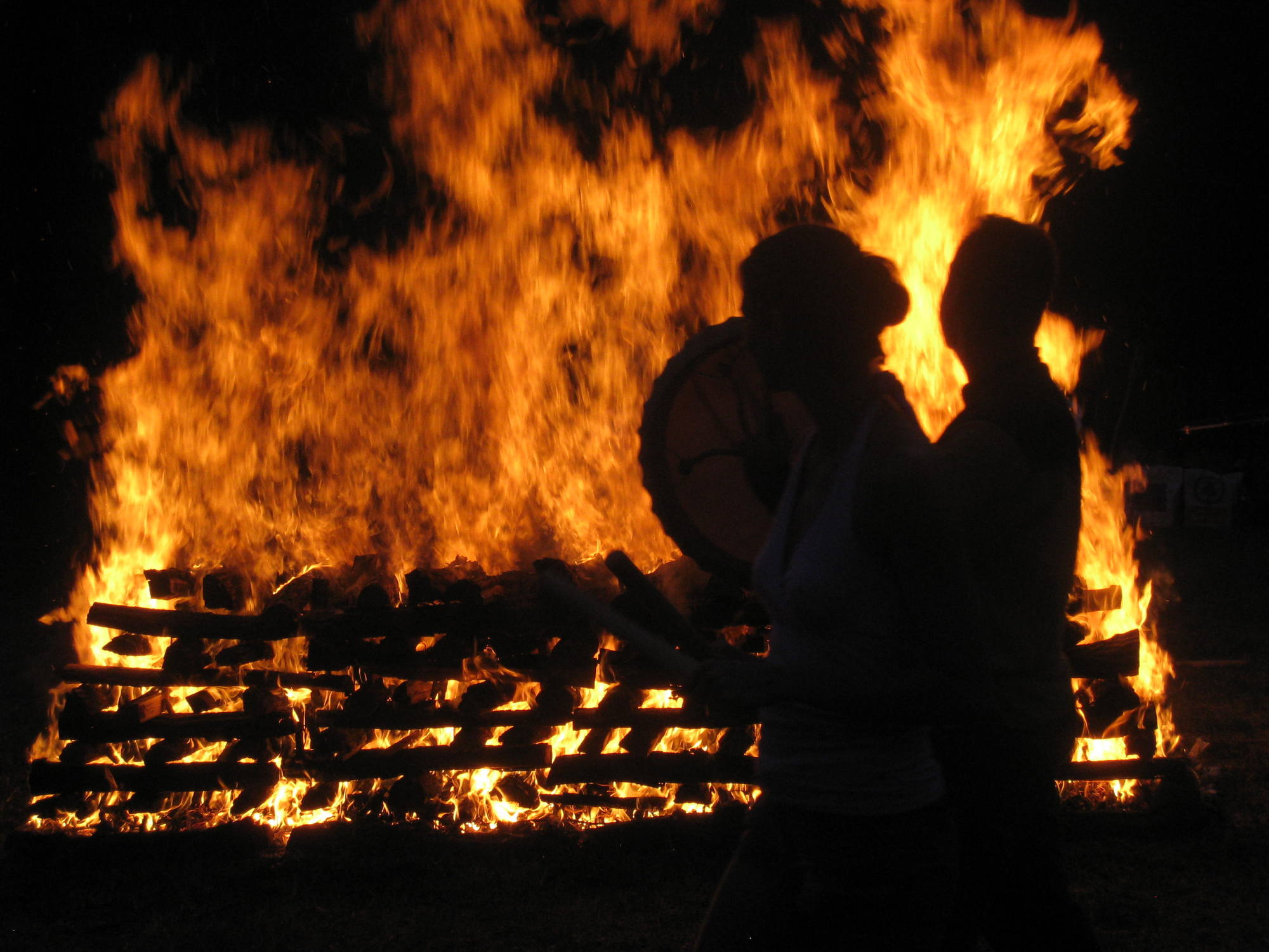 Two figures silhouetted beside a large burning pyre