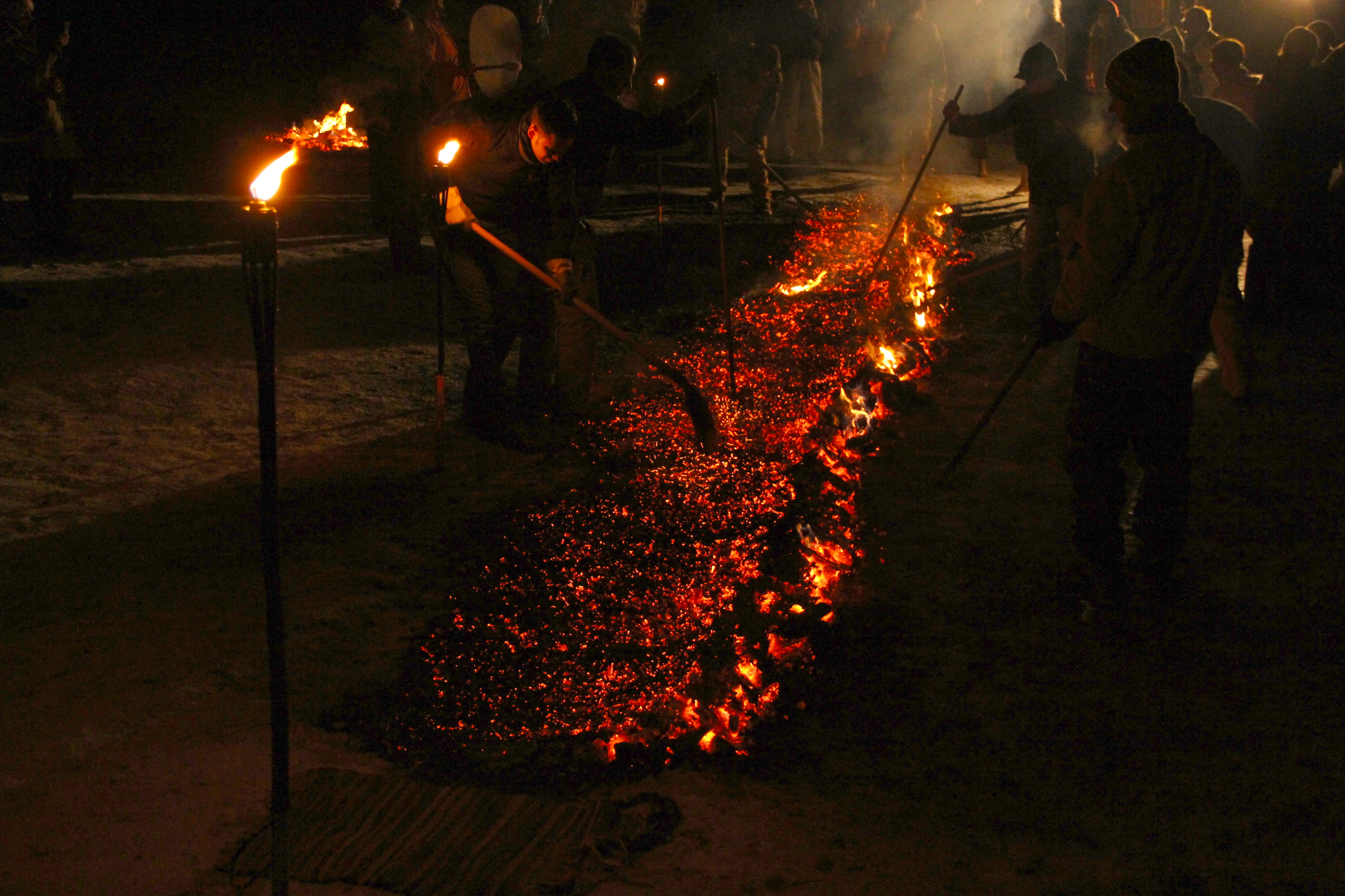 A firekeeper preparing a long twelve-metre bed of embers