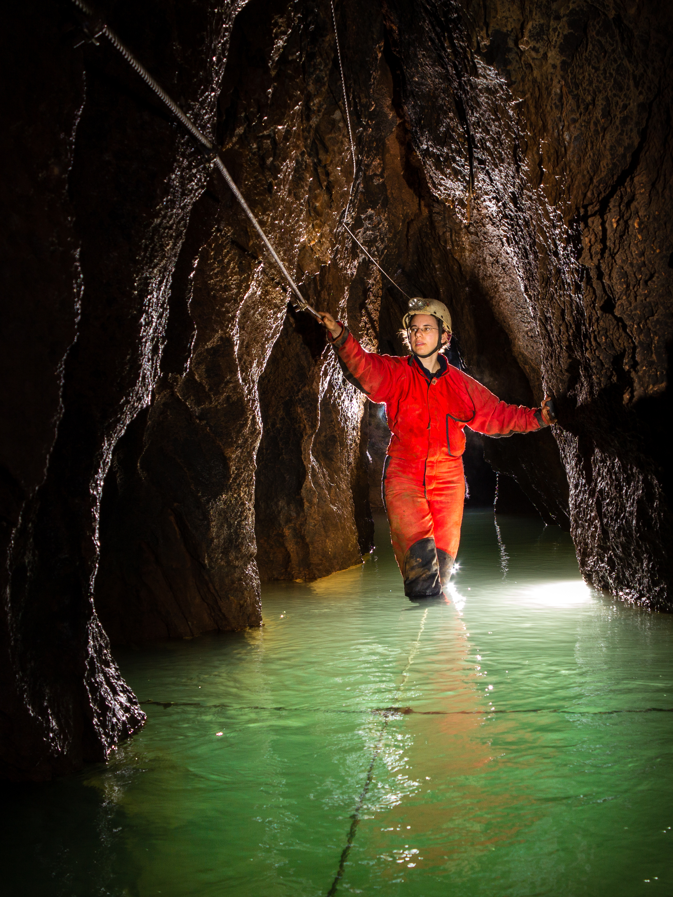 A caver moving through a narrow rock passage filled with water