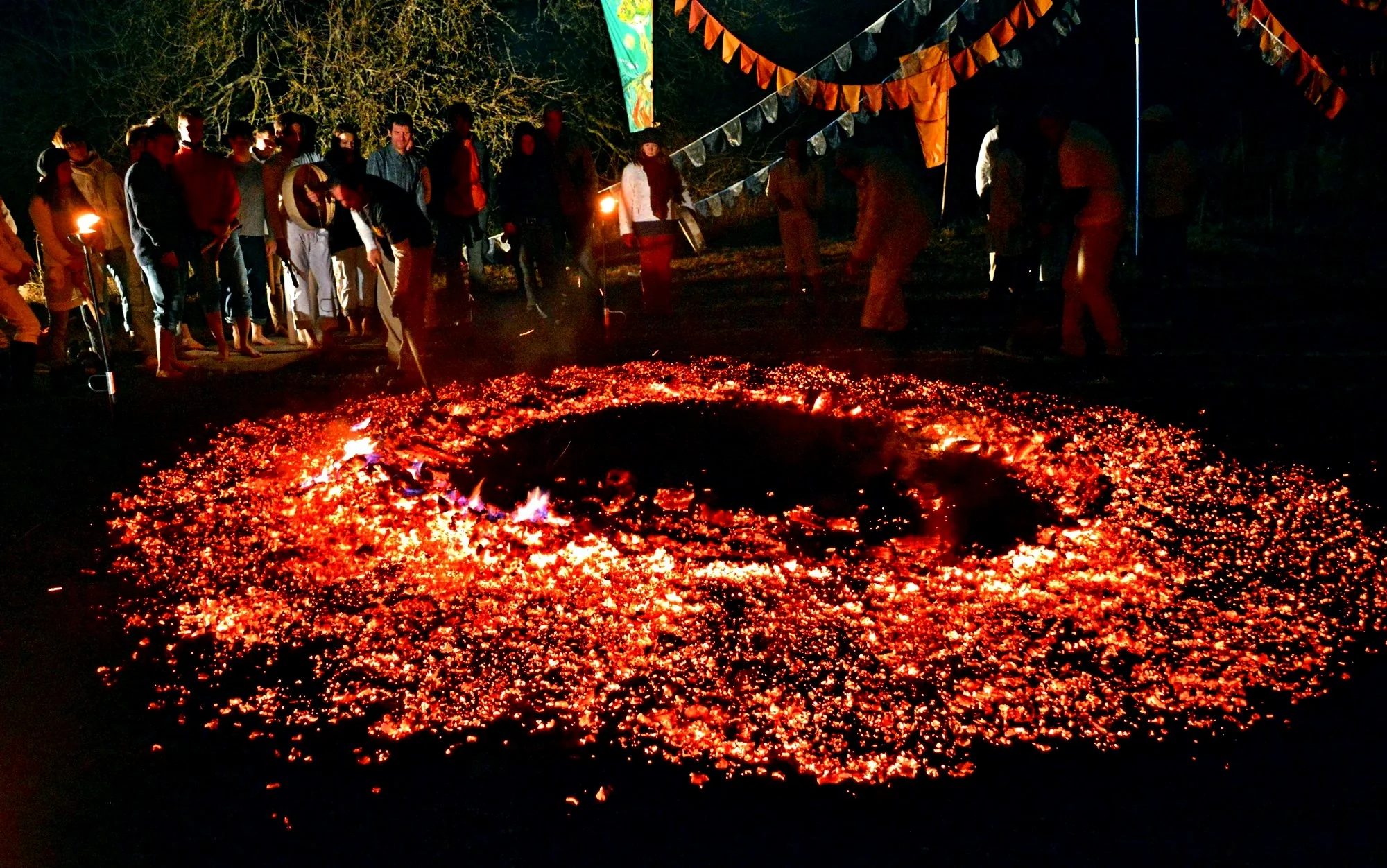 A circular ember path glowing beneath ceremonial flags