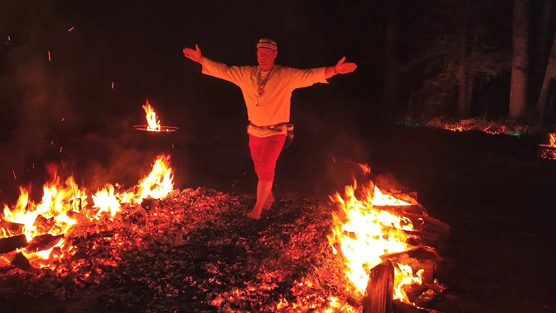 A blindfolded firewalker moving between flames with open arms