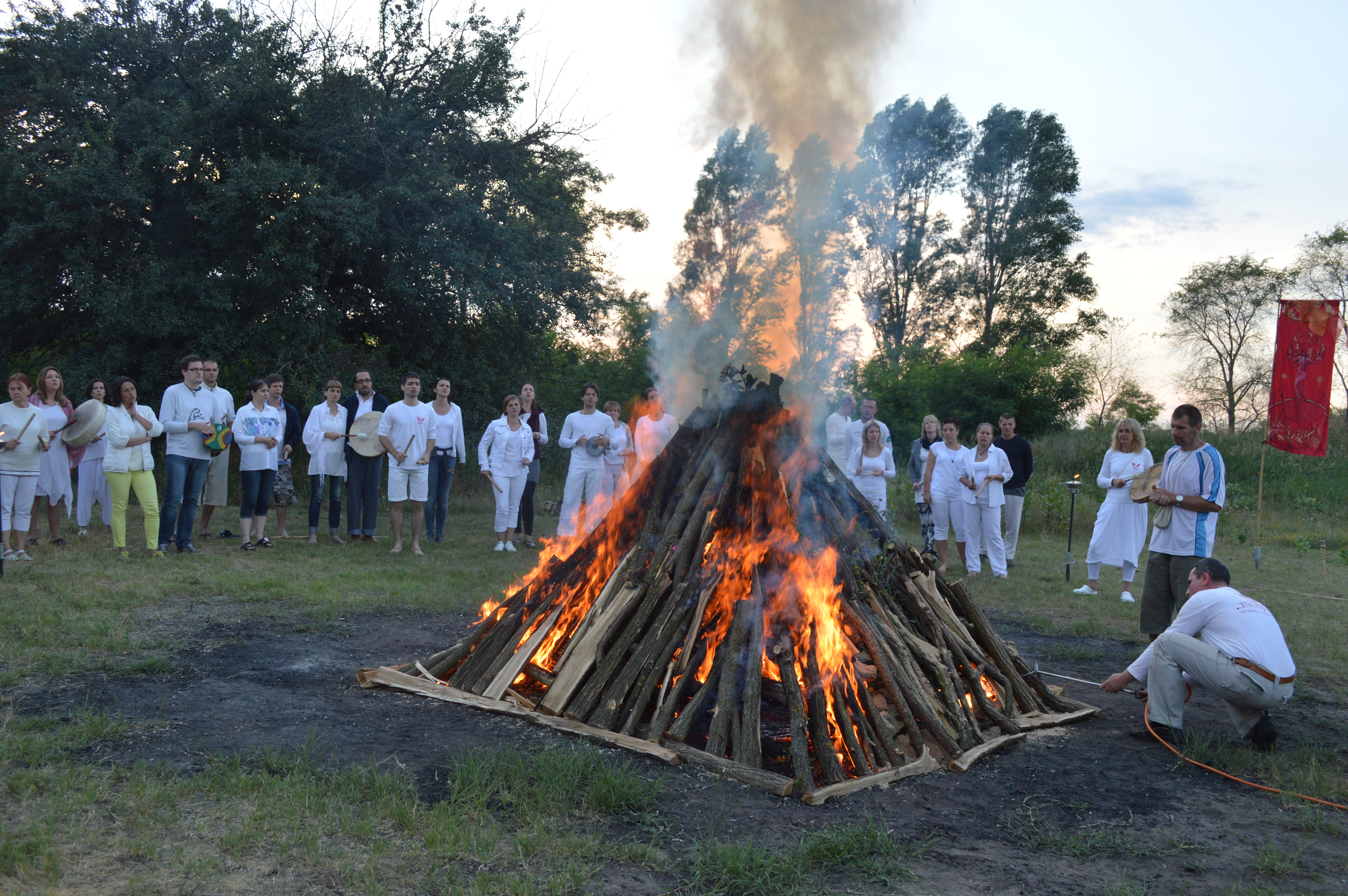 A man lighting a pyramid-shaped ceremonial pyre surrounded by participants
