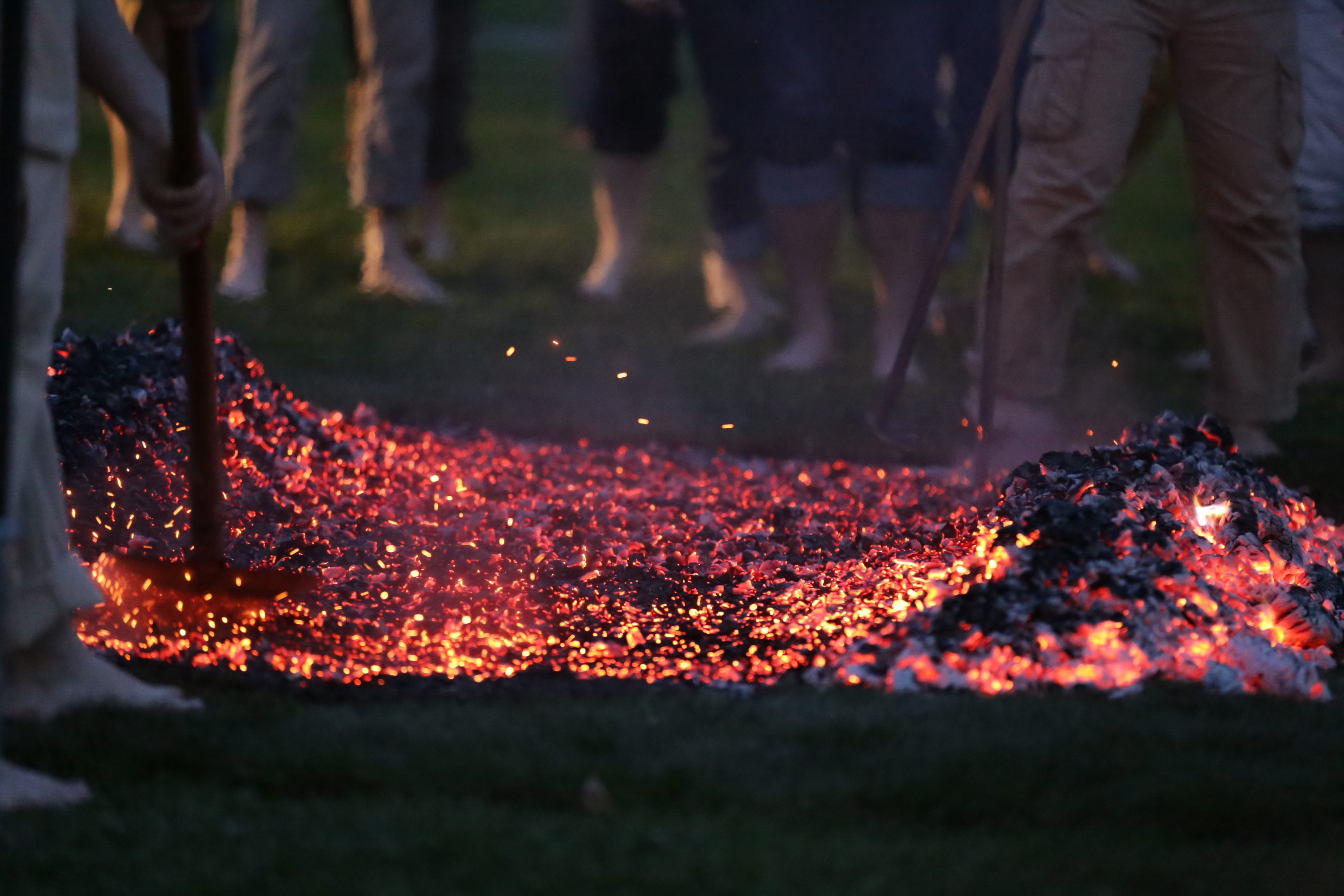 Fire tenders raking glowing embers into a walkable fire bed